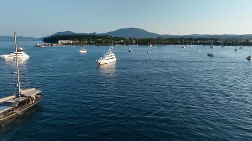 Aerial drone view of luxury yachts and sailboats anchored in a calm blue sea bay near a coastal city