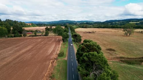 Forward flight over straight road through agricultural fields with hills
