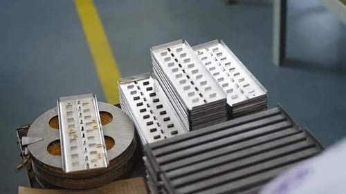 Scène d'assemblage industriel montrant des plateaux métalliques contenant des composants électroniques de précision et un support