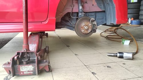 A small red car is seen in a workshop, undergoing a tire change.