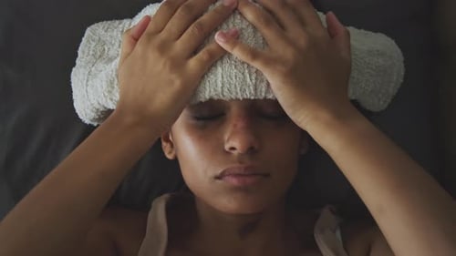 Fille fiévreuse avec du mascara taché et une serviette humide sur le front allongée dans son lit