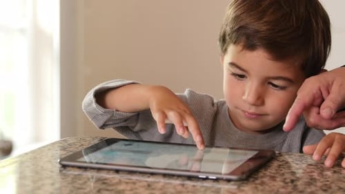 Boy Uses Tablet Device with Adult Supervision Indoors