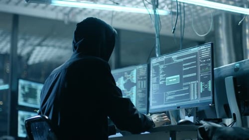 Hooded Hacker Breaks into Corporate Data Servers from His Underground Hideout. Place Has Dark Atmos