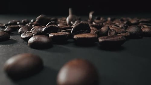 Ausgeschnittene Ansicht gerösteter Kaffeebohnen, die über eine schwarze Oberfläche fallen