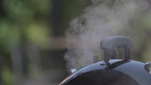 Smokes Came Out From A Barbecue Grill Lid With Handle In Bokeh Background. - Selective Focus Shot