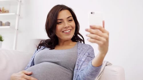 Happy pregnant woman uses smartphone video chat to connect at home
