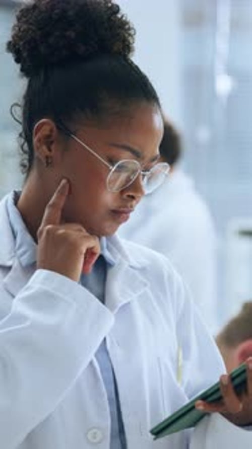 Thoughtful Woman in Lab Coat Uses Tablet