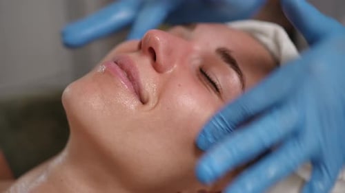 Woman receiving facial treatment with blue gloved hands