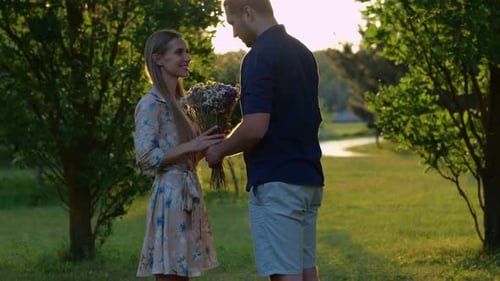 Handsome Young Man Giving Flowers to His Beautiful Happy Woman Standing Outdoor in Park on Sunset