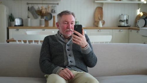 Senior Man Using Smartphone on Couch at Home