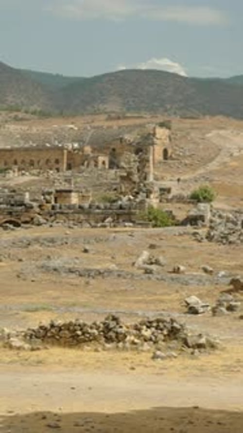 Vidéo verticale. Ruines de la ville antique au pied de la montagne, herbe sèche et pierres éparpillées.