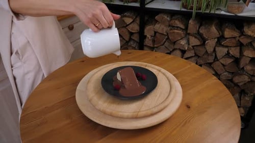 A Closeup of the Cook Pouring Liquid Chocolate on a Cake on a Plate in a Cafe
