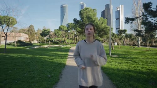 A Young Woman Enjoys a Leisurely Jog in a City Park Surrounded By Modern Buildings