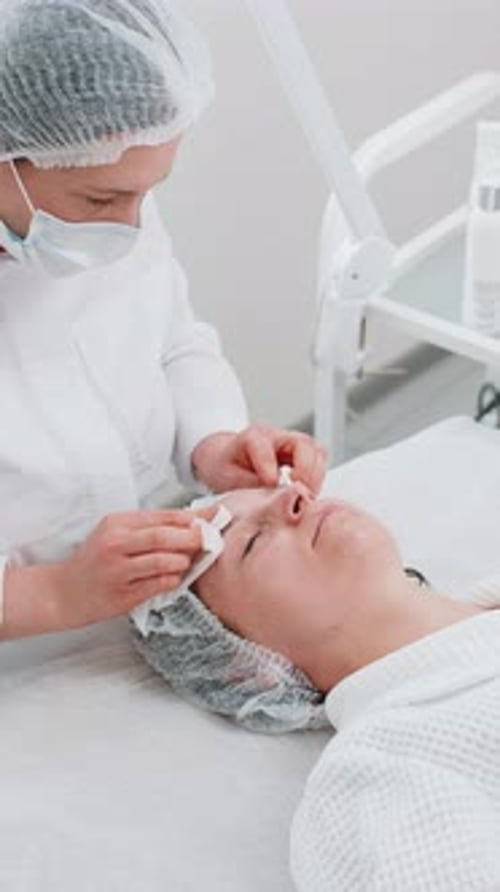 Cosmetologist Doctor Wipes Woman Face and Neck Cleaning Procedure with Cotton Pads in Beauty Clinic