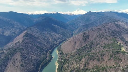 Snow-capped mountains and lush valleys surround a winding river under a clear blue sky