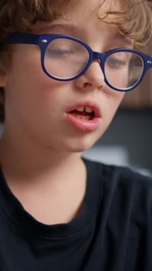 Closeup of a Young Boy Wearing Blue Glasses Concentrating Deeply While Writing with a Pen on Paper