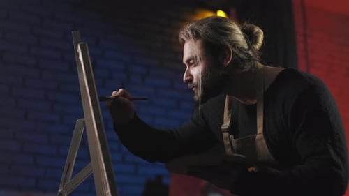 Man in Apron Drawing with Brush on Easel in Art Studio