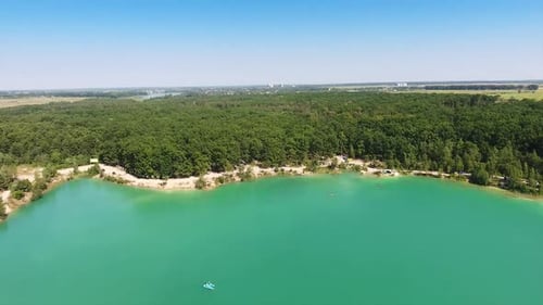 Deep blue lake with white sandy banks around. Green forest covering the waterfront. Cityscape