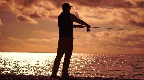 Man Standing on Pier Holding a Fishing Rod and Preparing to Cast It Into Sea Ocean at Warm Sunset