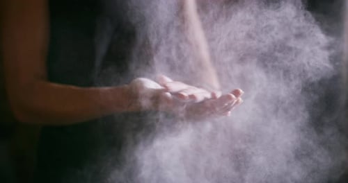 An unrecognizable woman dusting her hands with chalk powder at the gym