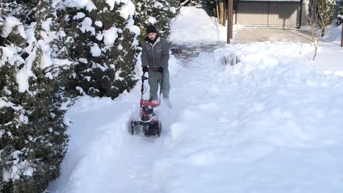 Man Clearing a Narrow Backyard Path with a Snow Blower Removing Fresh Snow After a Storm While