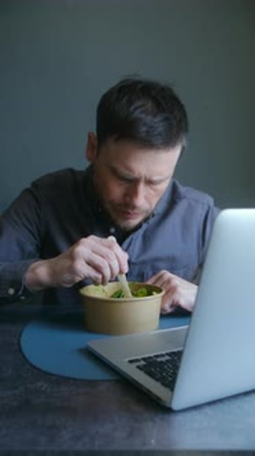 Man Eats Salad While Looking at Laptop Screen