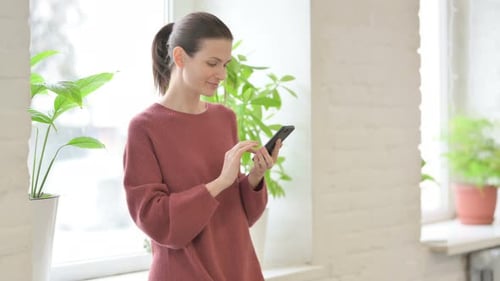 Woman Using Smartphone Indoors by Bright Window