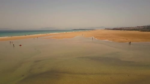 AERIAL ZOOMING OUT. People walking along beach and lagoon.