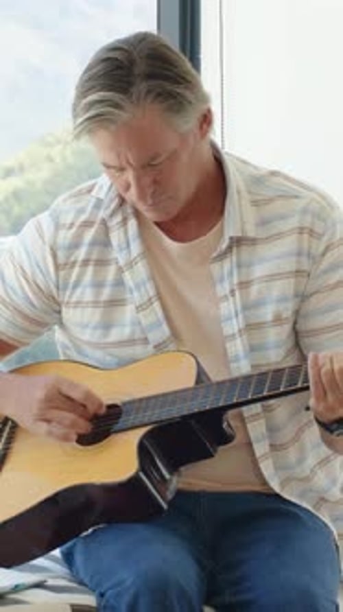 Vidéo verticale : S'installant à la guitare, homme en chemise s'entraînant à pincer et à gratter près de la fenêtre avec des tablatures