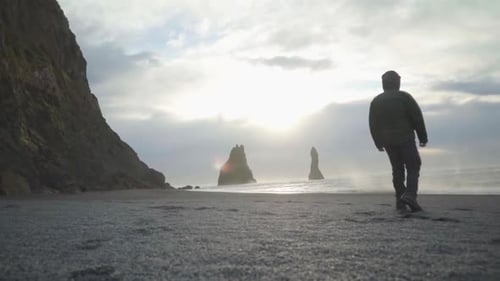 a person tourist walking on the sand of black beach towards rocks in the sea of Reynisfjall beach