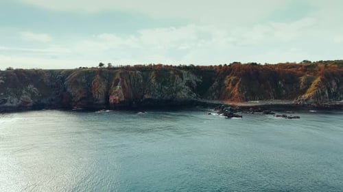 Distancing from the rocky shore of the sea. Drone footage over the peaceful waterscape.