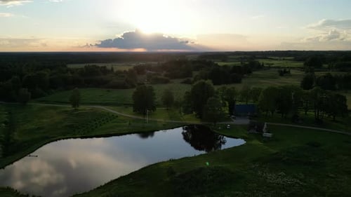 Time lapse of a sunset with green fields and trees and a small lake nearby a single family house