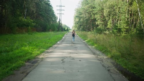Distant View Lady Walking On Tarred Road Surrounded By Forest And Power Lines