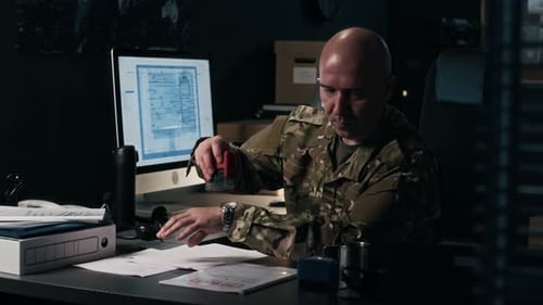 Military Man Reviews Documents in Office at Night