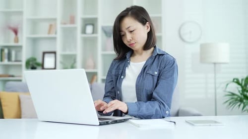 Adult asian businesswoman typing on laptop while sitting in home office. Female freelancer works