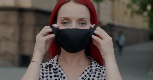 Woman Puts on Black Face Mask Outdoors