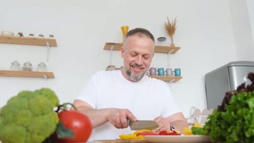 Man Happily Cuts Colorful Vegetables in Kitchen