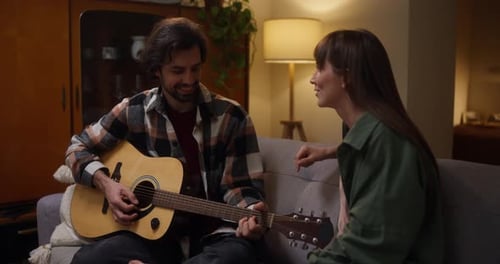 Man plays guitar with woman singing on couch