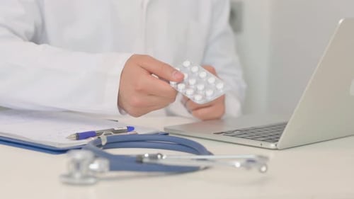 Close up of Doctor Showing White Strip of Pills Near Laptop
