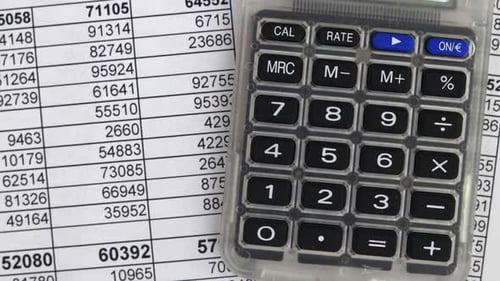 Taschenrechner, der auf einer Finanztabelle mit Zeilen numerischer Daten liegt