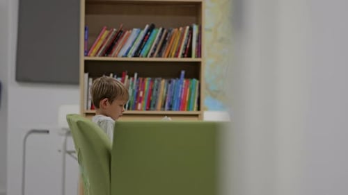 kleiner Junge liest ein Buch auf einem Stuhl in der Bibliothek