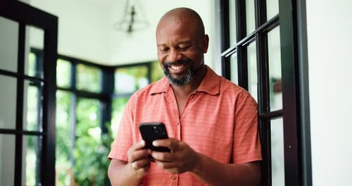 Smiling Man Uses Cell Phone Indoors near Window