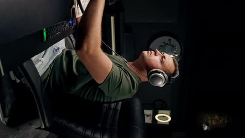 a focused male sound engineer wearing headphones sits at a mixing desk recording new track