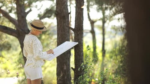 Beautiful Girl Artist in the Summer in the Forest Draws a Picture Background Landscape and Creates