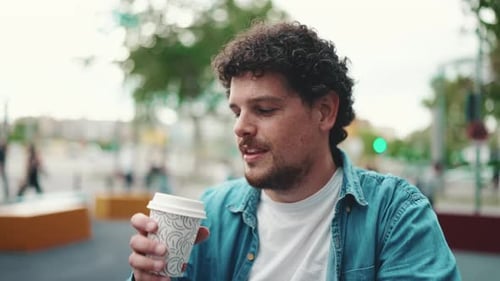 Close-up of man sitting and drinking coffee on busy street modern city background