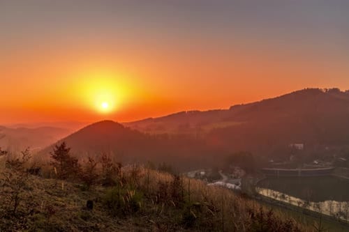 Zeitraffer bei Sonnenuntergang, wenn die Sonne hinter Hügeln und Bergen voller Bäume und sich bewegender Wolken steht, hinter denen