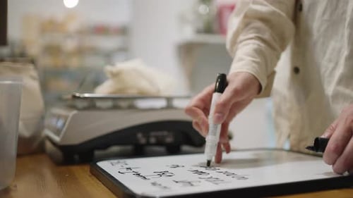 Woman Weighs and Writes Down the Weight of the Purchased Product with a Marker on a Blackboard in an