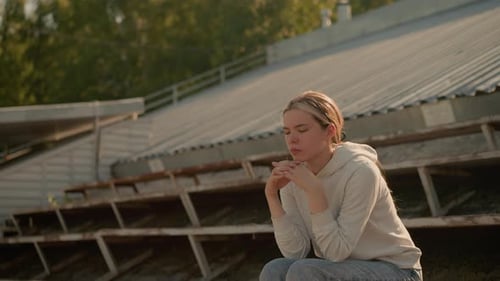 Contemplative Woman Sitting on Rustic Stadium Bleachers in Thoughtful Expression