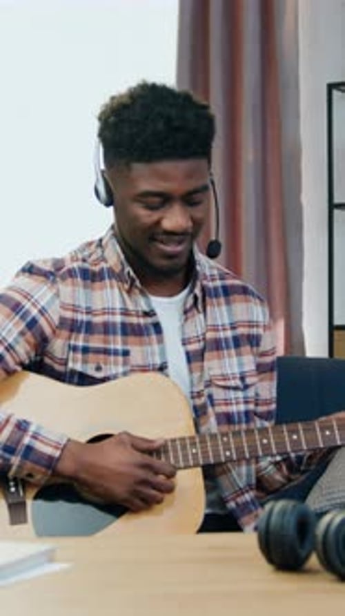 Smiling Man Plays Guitar and Speaks into Headset