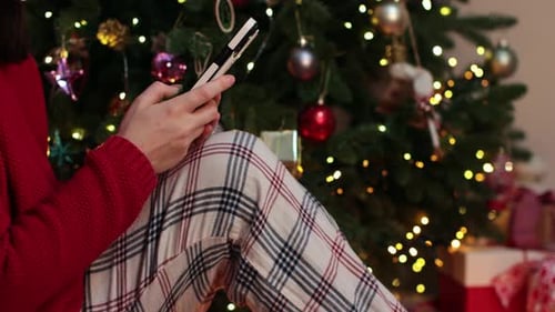 Woman Using Phone by Christmas Tree